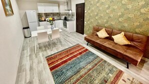 Un salon moderne avec un canapé en cuir marron, un tapis à motifs et un coin repas comprenant des chaises blanches et une table blanche.