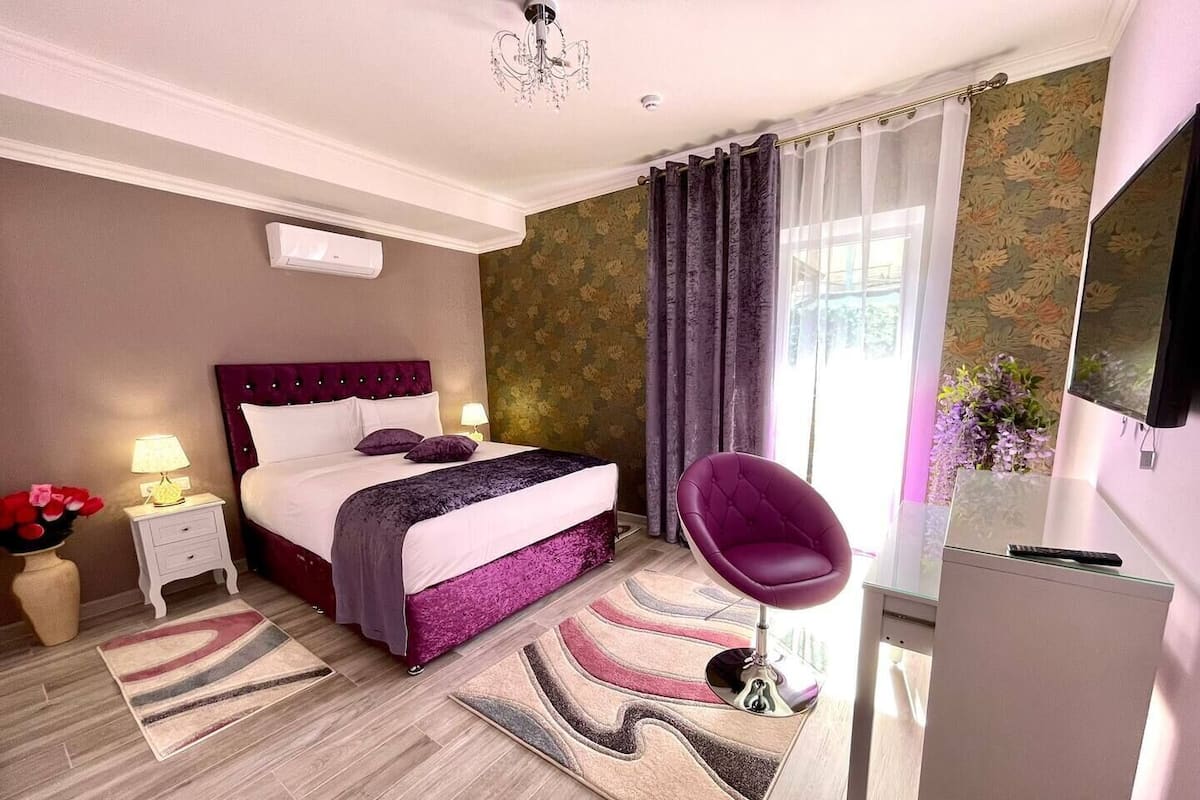 Een slaapkamer met een bed, nachtkastjes, een stoel, een televisie en een raam met gordijnen.