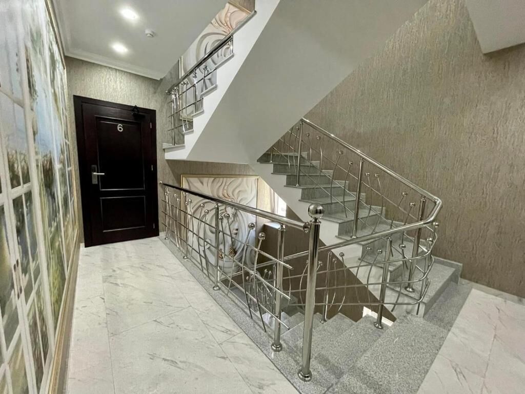 Un intérieur moderne avec un escalier en marbre, une porte noire et un mur orné d’un motif texturé.
