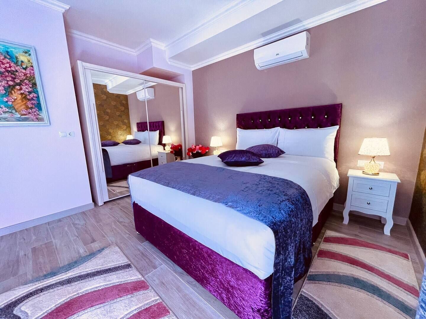 A hotel room with a large bed, a nightstand, a lamp, and an air conditioning unit.