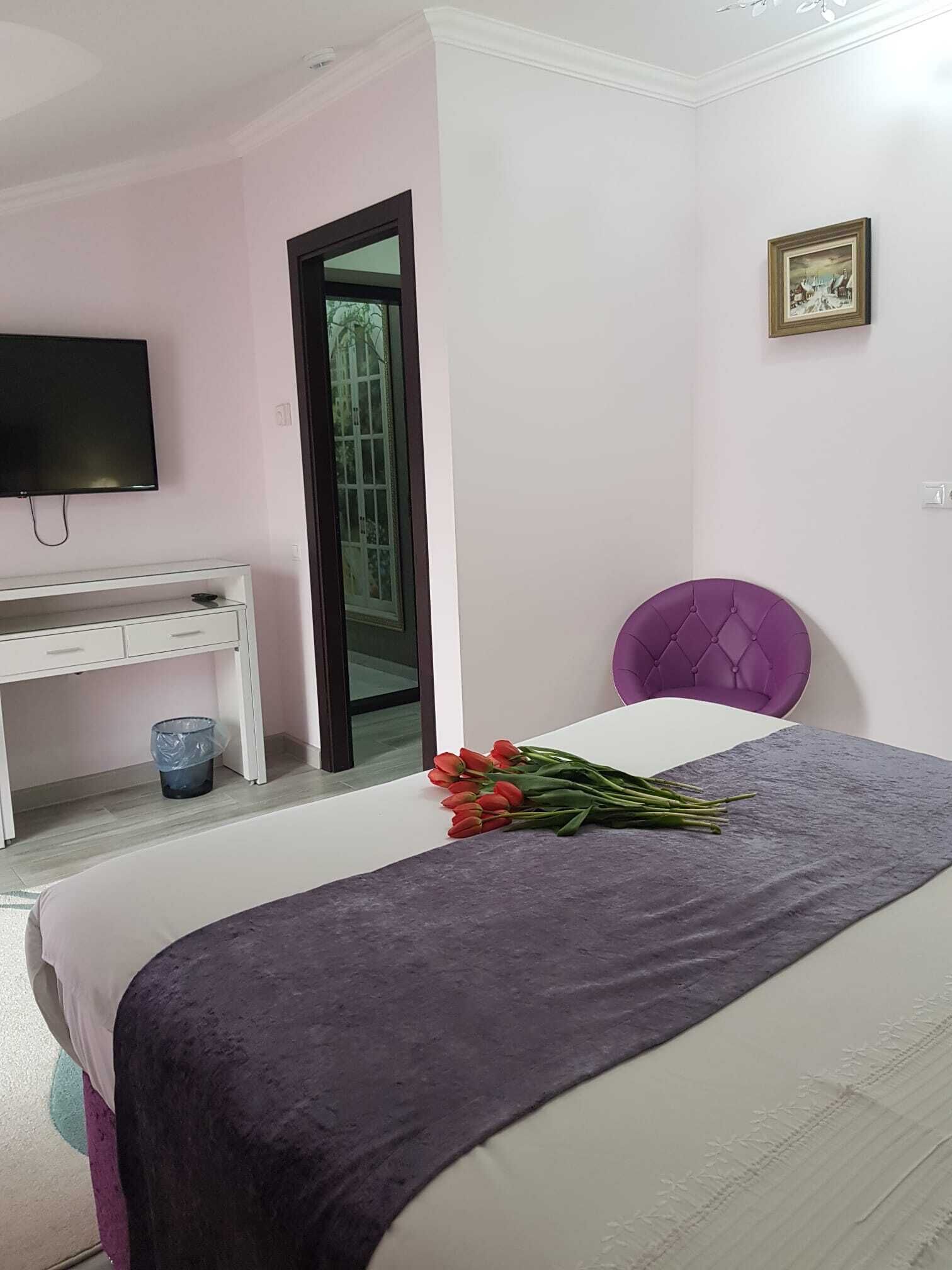 A bedroom with a bed, a desk, a television, and a window.