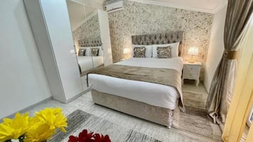 Een slaapkamer met een groot bed, een kledingkast, een spiegel en een nachtkastje met een lamp.