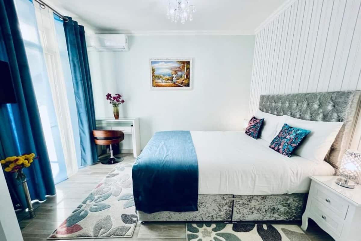 Een slaapkamer met een bed, nachtkastje, kaptafel en een schilderij aan de muur.