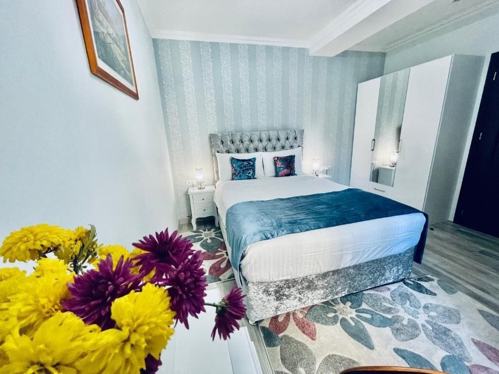 A bedroom with a bed, a nightstand, a mirror, and a floral arrangement.