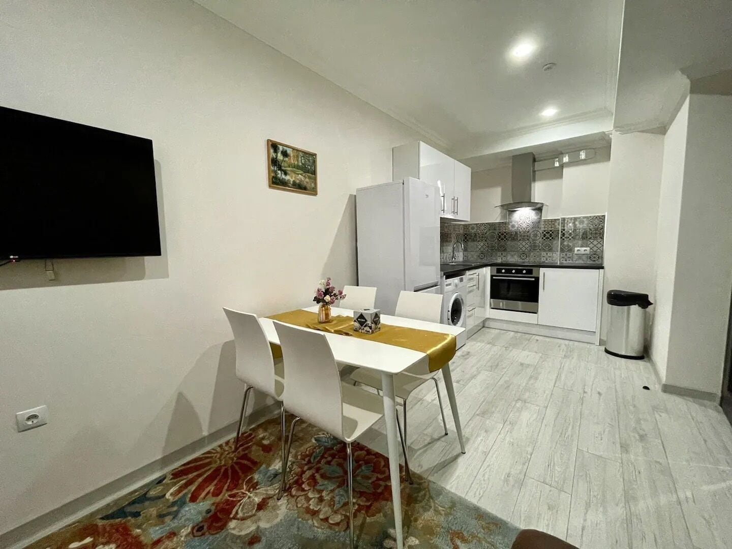 A compact living space with a dining area, a kitchen, and a flat-screen TV mounted on the wall.