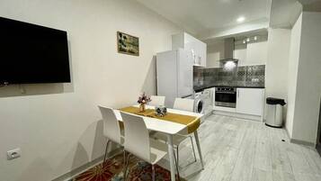 A compact living space with a dining area, a kitchen, and a flat-screen TV mounted on the wall.