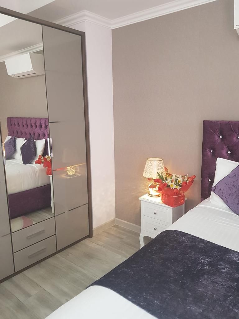 Een slaapkamer met een bed, nachtkastje met lamp, spiegel en garderobe.