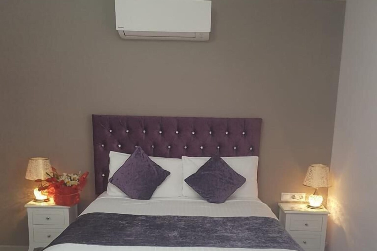 Un lit avec une tête de lit capitonnée, deux tables de chevet avec des lampes et un climatiseur fixé au mur.