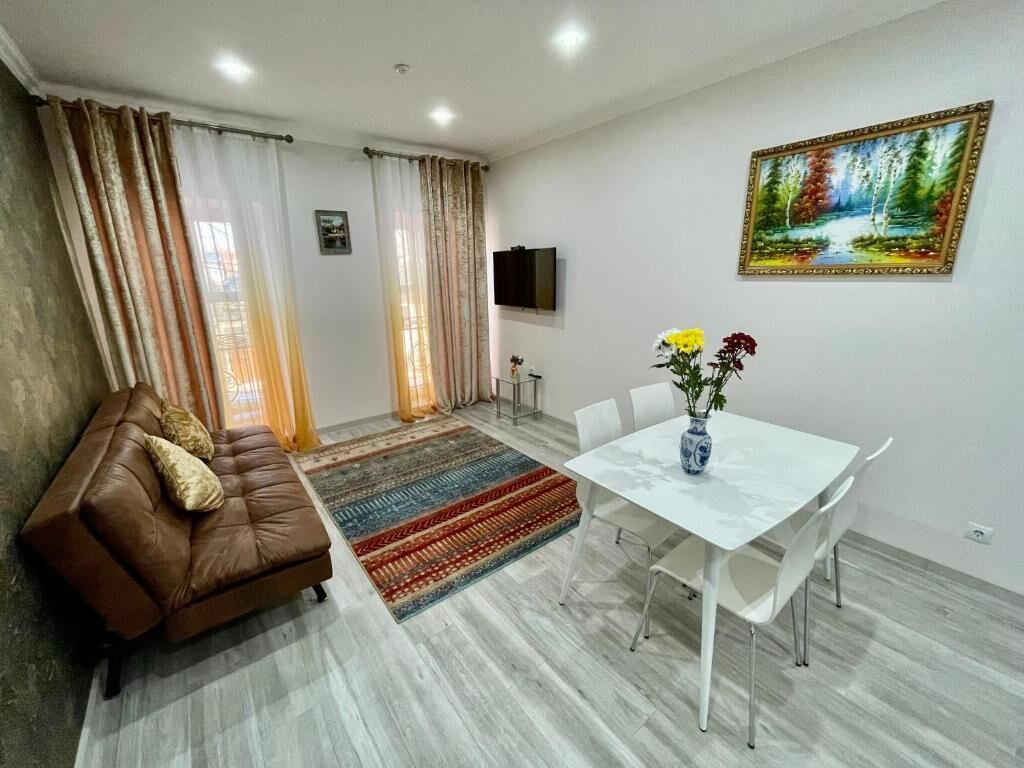 Un salon comprenant un canapé, une table à manger avec des chaises, un téléviseur fixé au mur et un tableau au-dessus de la table.