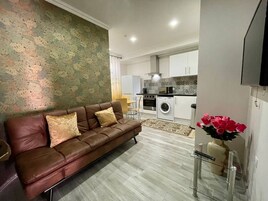 Una sala de estar con un sofá de cuero marrón, un papel tapiz estampado y una cocina al fondo.