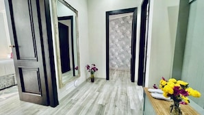 Un couloir avec un plancher en bois, un miroir et un vase rempli de fleurs.