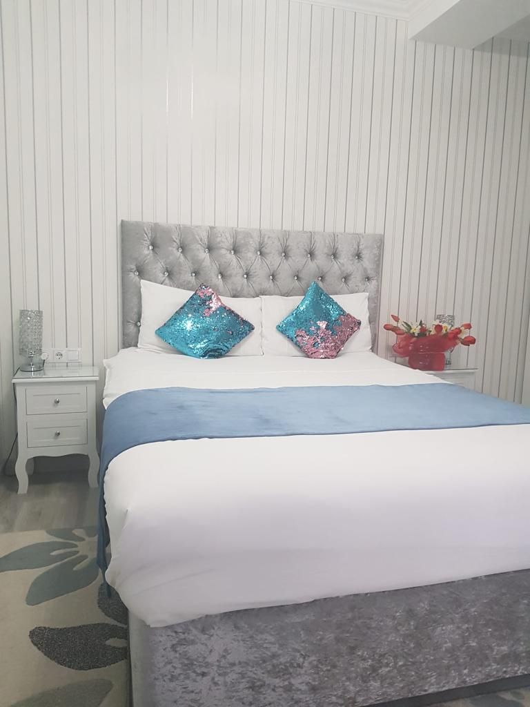 A bed with a tufted headboard, two decorative pillows, a bedside table with a lamp, and a vase with flowers.