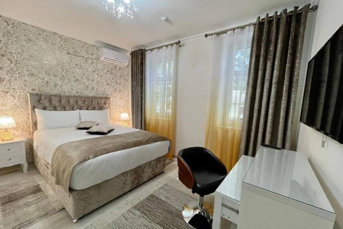 Een slaapkamer met een bed, nachtkastje, lamp, stoel, bureau en een flatscreen televisie.