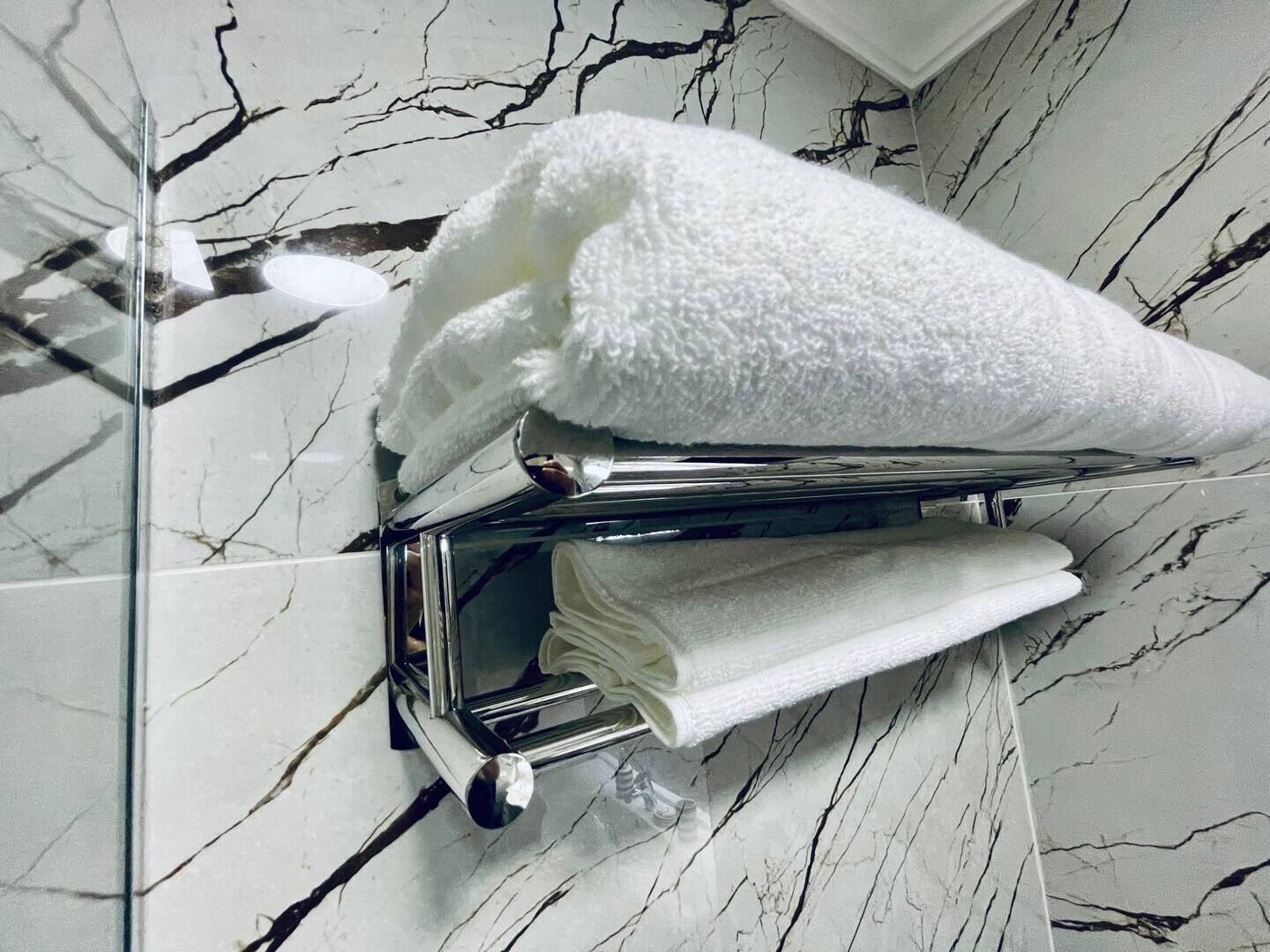 En handduksvärmare med två vita handdukar på, placerad framför en vägg av marmor.