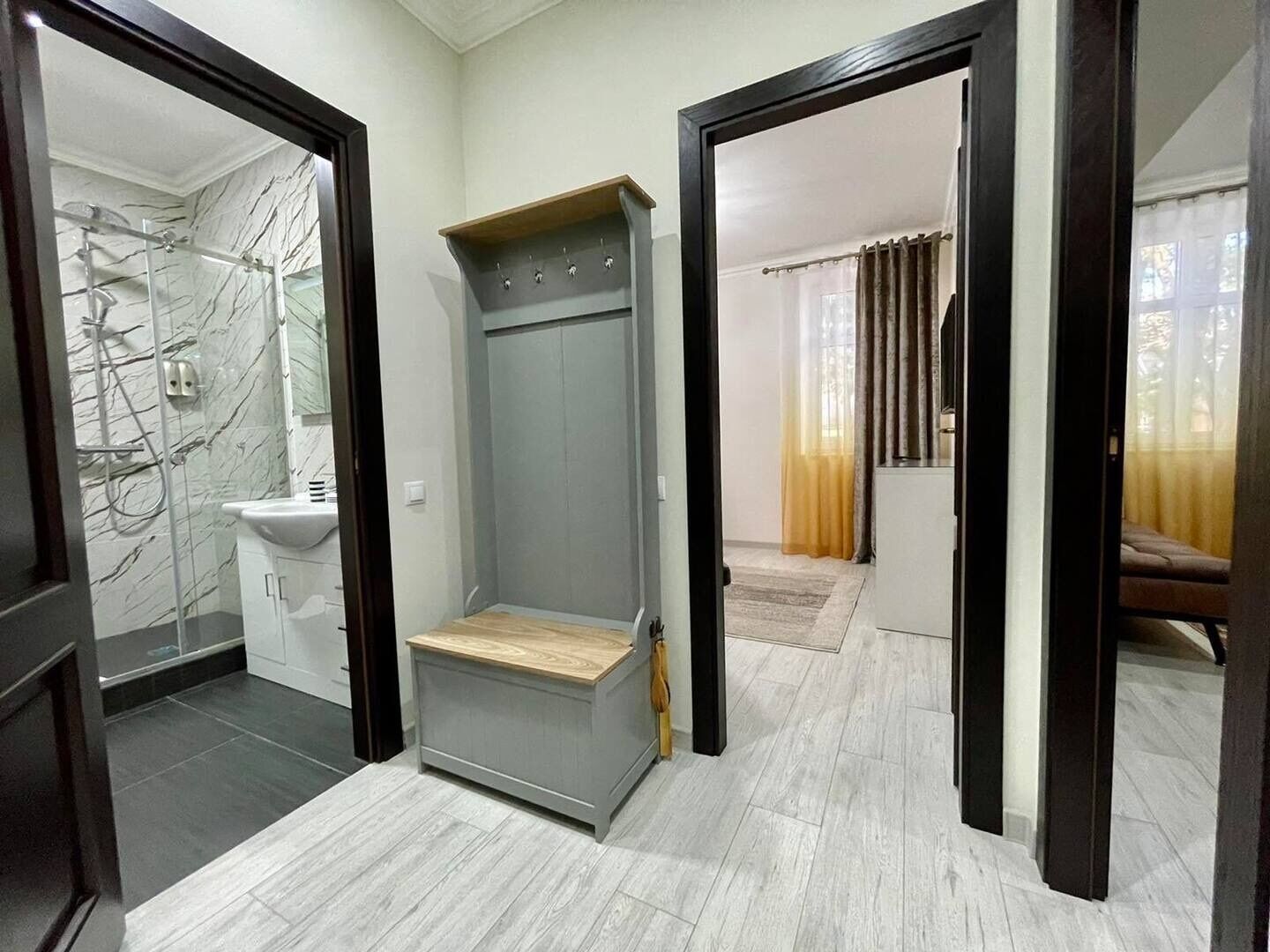 Une salle de bain avec un mur en marbre, un lavabo et une douche. Un banc en bois se trouve au centre de la pièce.