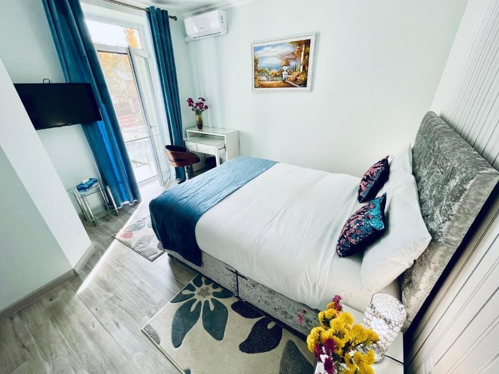 Un dormitorio con cama, escritorio, silla, televisor y ventana con cortinas.