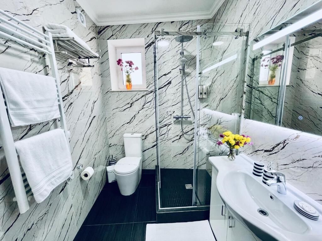 Et badeværelse med en marmorvæg, et brusekabine i glas, en hvid vask og et toilet.