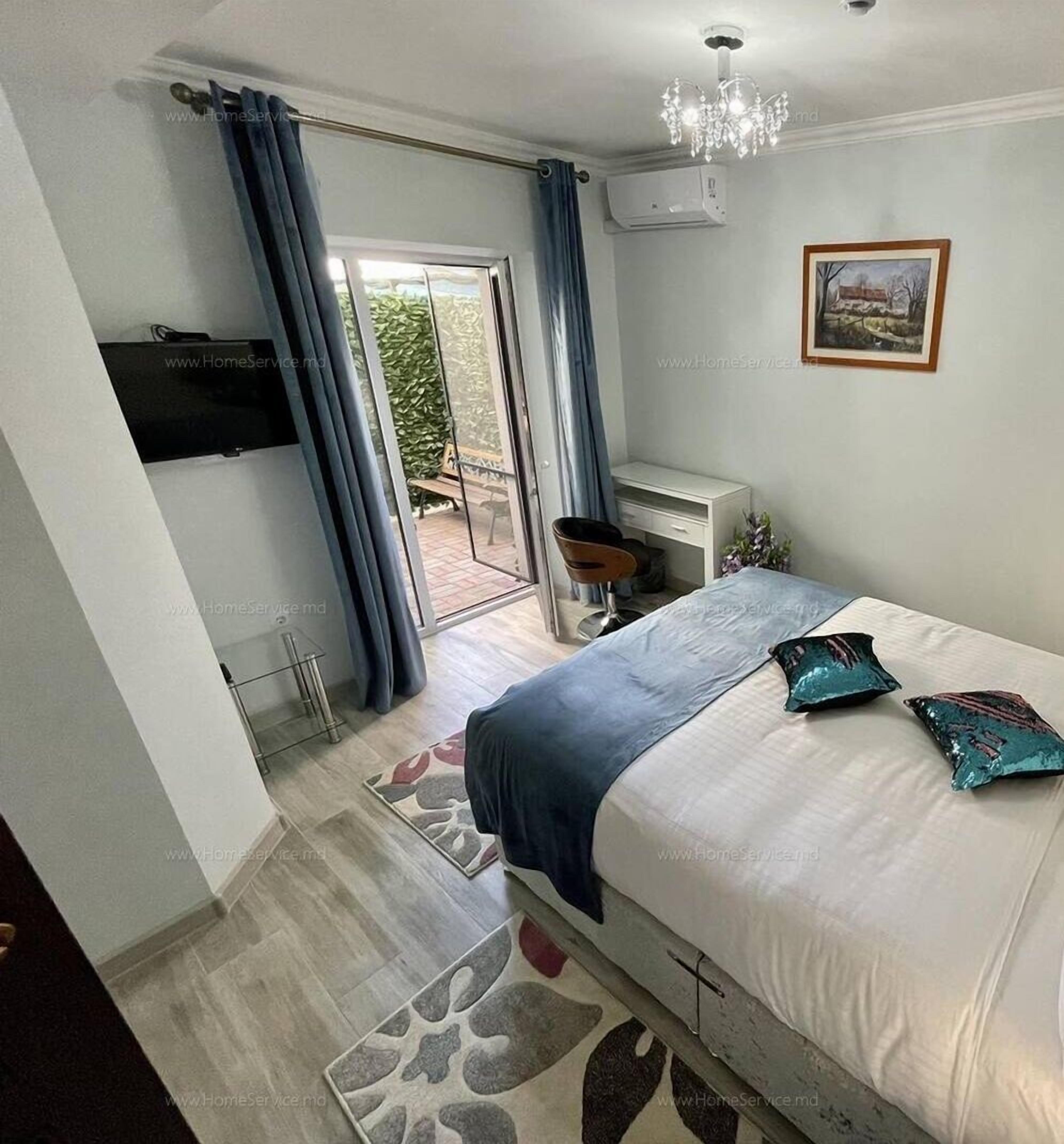 A bedroom with a bed, a desk, a chair, a television, and a sliding glass door leading to an outdoor area.