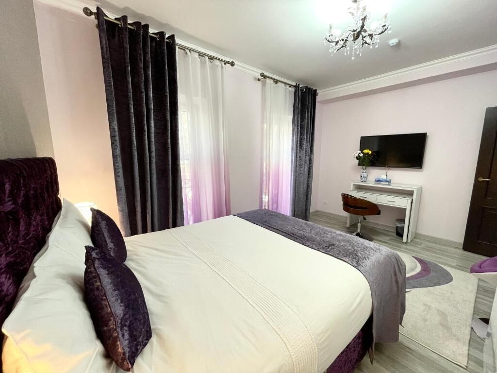 A bedroom with a bed, a desk, a chair, a TV, and a chandelier.