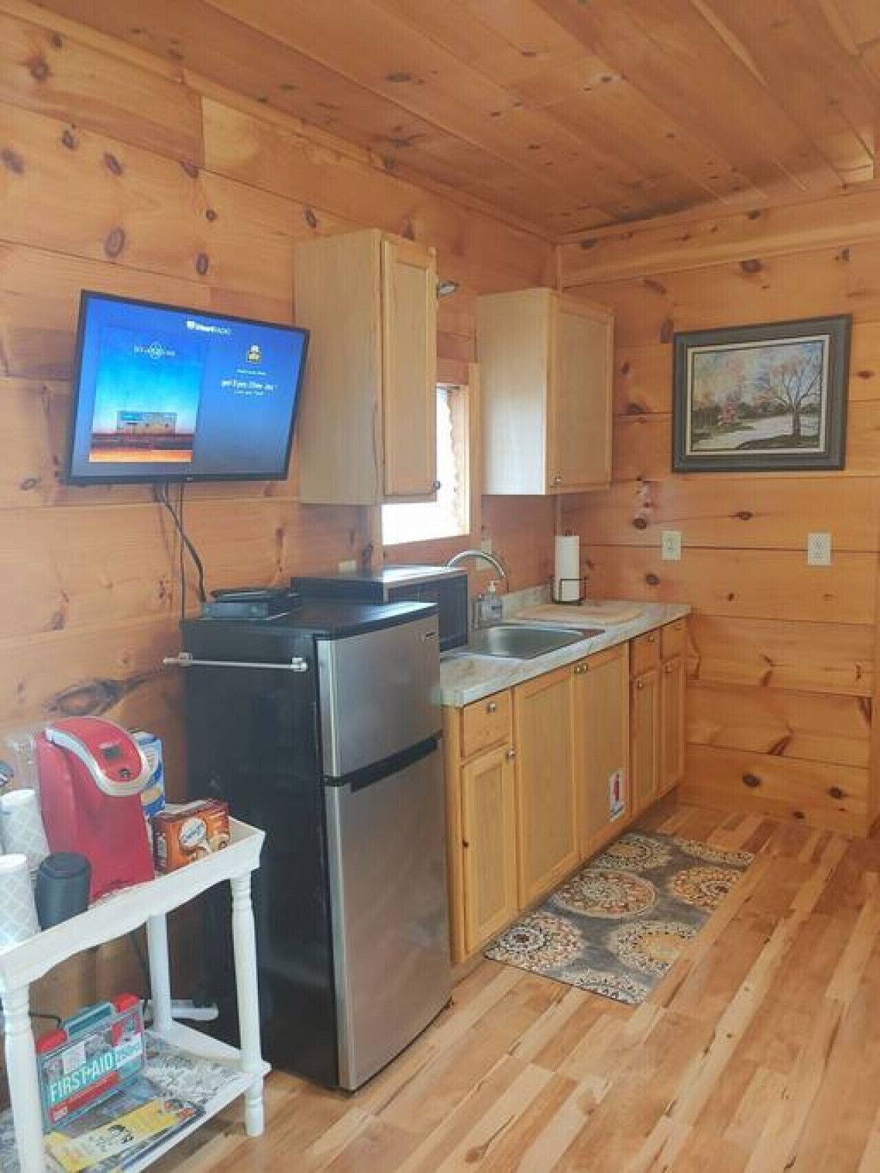Cocina compacta con paredes de madera, un refrigerador de acero inoxidable, un lavamanos y un televisor de pantalla plana montado sobre la encimera.