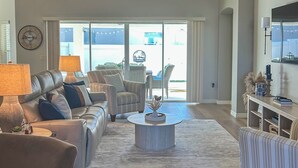 A modern living room with a leather sofa, striped armchairs, a round coffee table, and a large window with a view of the outside. - Private Lanai & Pool Access: Home in the Villages! (The Villages)