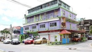 A multi-story building with a purple and green facade, a visible storefront, and several parked cars. - Quality Inn Suites, Guyana (Georgetown)