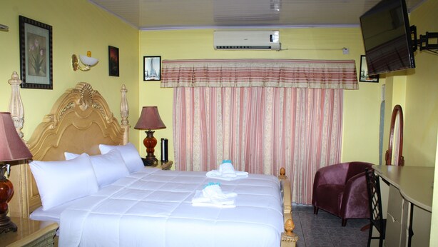 A hotel room with a large bed, a desk, a chair, a TV, and an air conditioning unit. - Quality Inn Suites, Guyana (Georgetown)