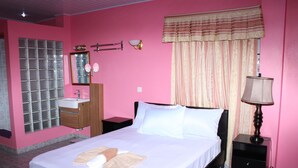 A hotel room with a bed, a nightstand, a lamp, a mirror, a window with curtains, and a bathroom with a sink and mirror. - Quality Inn Suites, Guyana (Georgetown)