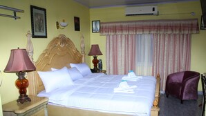 A hotel room with a large bed, two bedside tables, a chair, and a window with curtains. - Quality Inn Suites, Guyana (Georgetown)