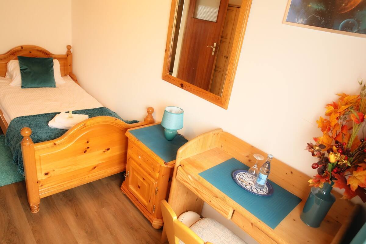 A bedroom with a wooden bed, a nightstand, a dresser, and a desk with a chair.