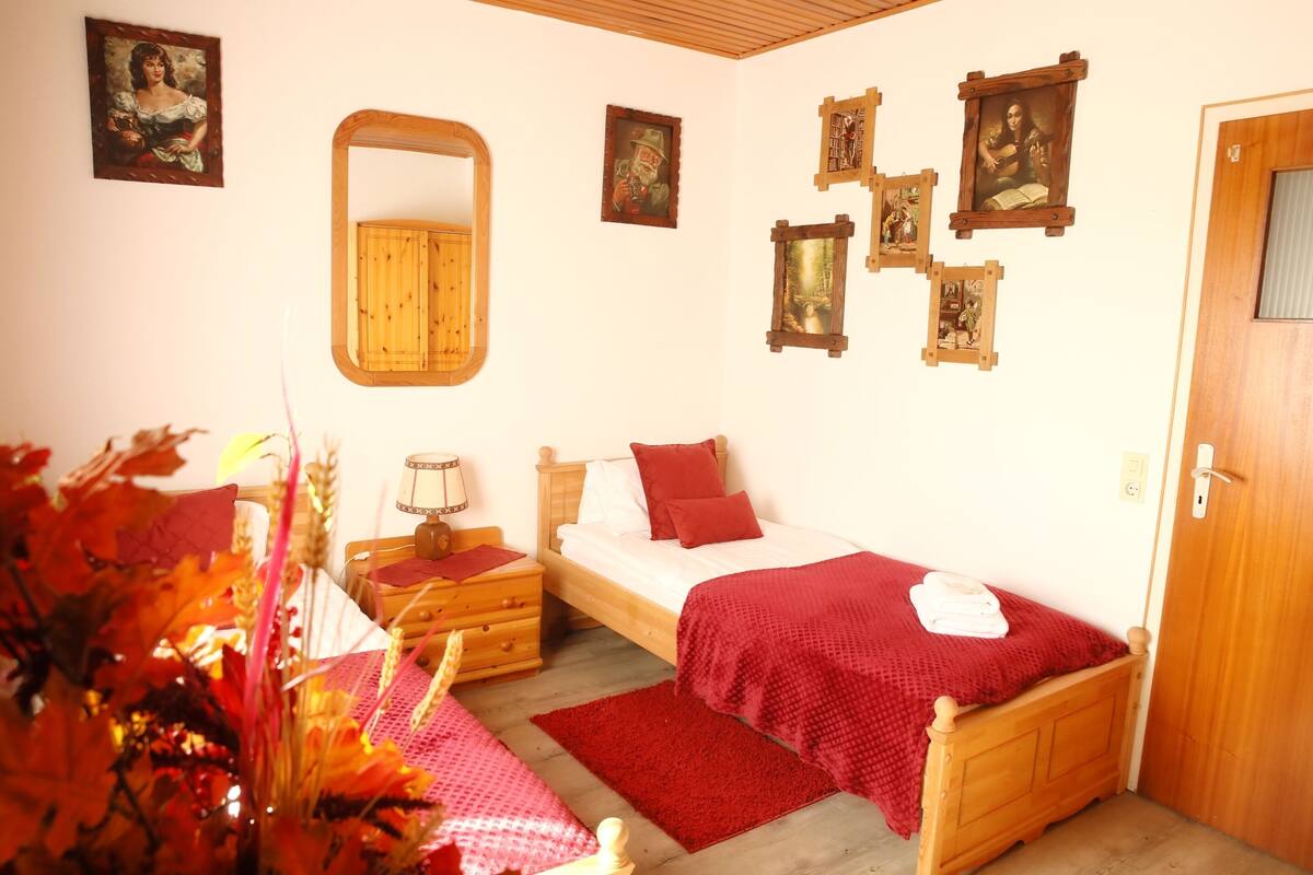 A bedroom with a wooden bed, a nightstand, a dresser, a mirror, and several framed pictures on the wall.