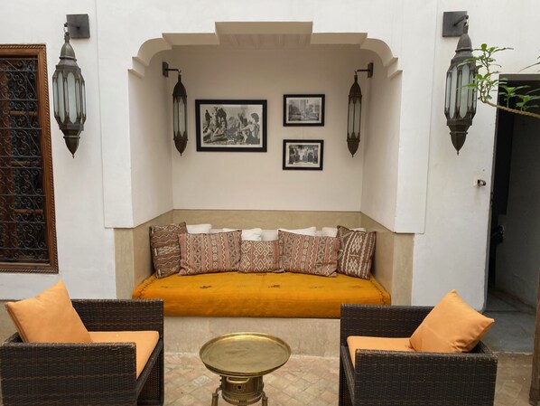 A cozy seating area with a sofa and two wicker chairs, a small round table, and decorative wall-mounted lamps. - Private Moroccan Riad • Rooftop Dinners & Pool • Luxury Experience (Marrakesh)