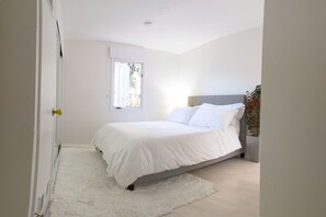 A bedroom with a bed, a window, a door, and a plant.