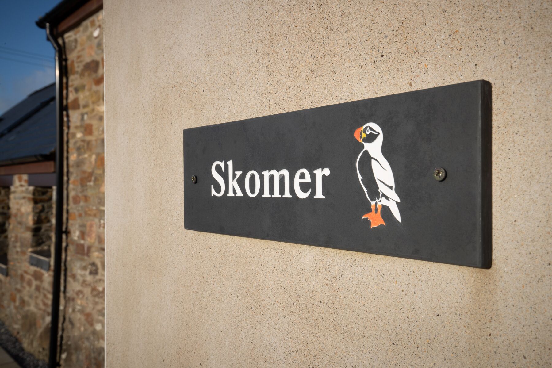 A sign with the name 'Skomer' and a penguin illustration.