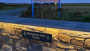 Opastekyltti, jossa lukee Rainbolts Hill Farm, ja taustalla näkyy kivimuuri sekä tie.