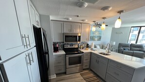 A modern kitchen with stainless steel appliances, a large island, and a view of the living area. - Complimentary Beach Service with 2 chairs and umbrella (Panama City Beach)