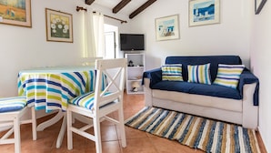Un salon comprenant un canapé, une table à manger avec des chaises, un téléviseur et des œuvres d’art accrochées aux murs.