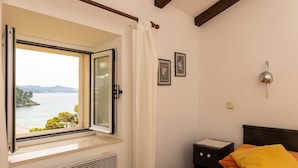Une chambre avec une fenêtre donnant sur un plan d’eau, un lit recouvert d’une couvre-lit à rayures, une table de chevet et un luminaire fixé au mur.