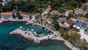 Vue aérienne d’une ville côtière avec un port de plaisance, des bâtiments en pierre et une végétation luxuriante.