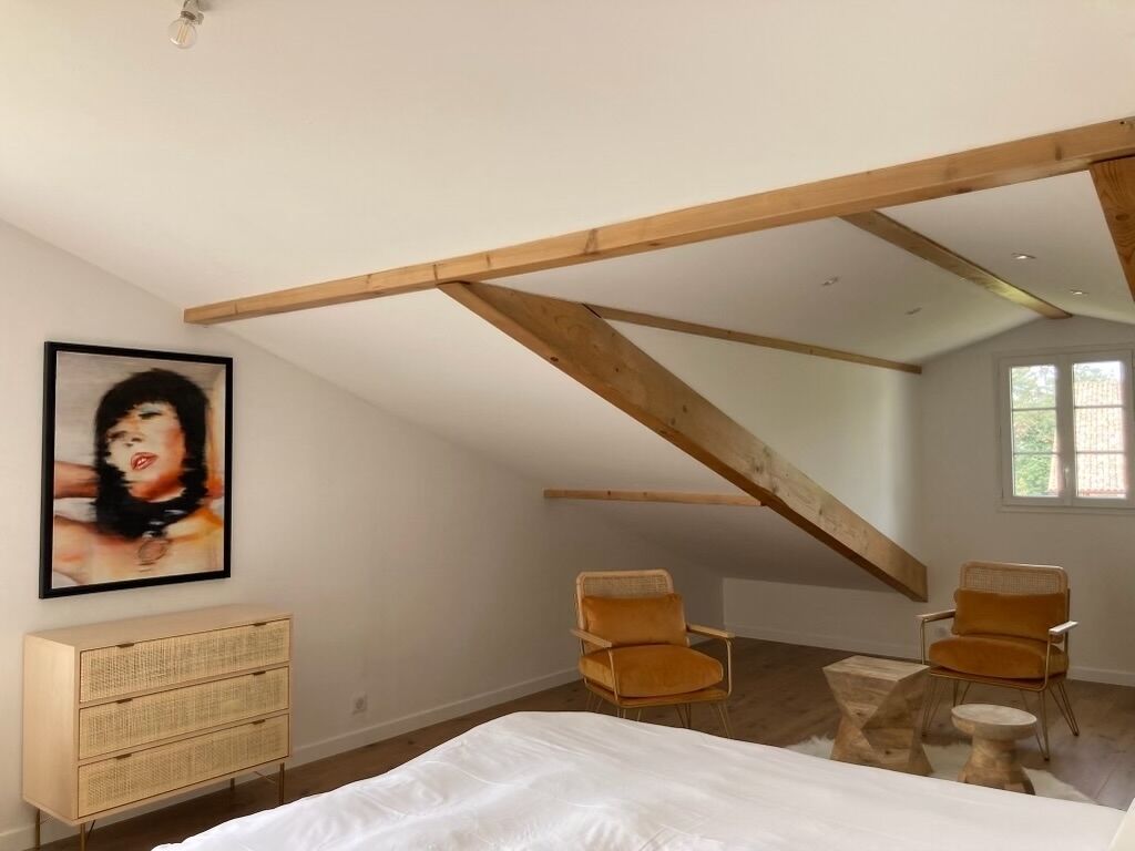 A bedroom with a sloped ceiling, a bed, two chairs, a dresser, and a framed picture on the wall.