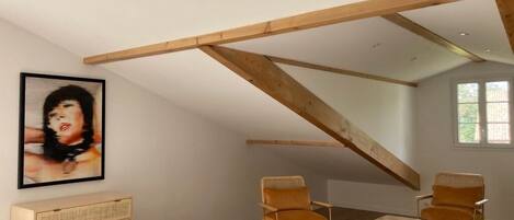 A bedroom with a sloped ceiling, a bed, two chairs, a dresser, and a framed picture on the wall.