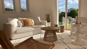 Una sala de estar moderna con un sofá blanco, una silla de mimbre, una mesa de centro redonda y una mesita auxiliar blanca.