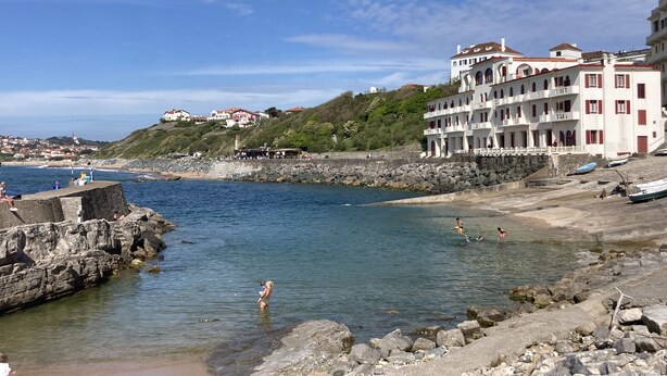 Un pueblo costero con un litoral rocoso, un muelle y edificios con balcones con vistas al mar.