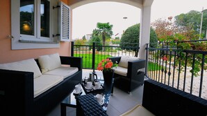 A balcony with wicker furniture, a table with a tray of cups and a flower vase, and a view of a garden and buildings in the background. - Villa Gea - Three Bedroom with Swimming Pool (Barban)