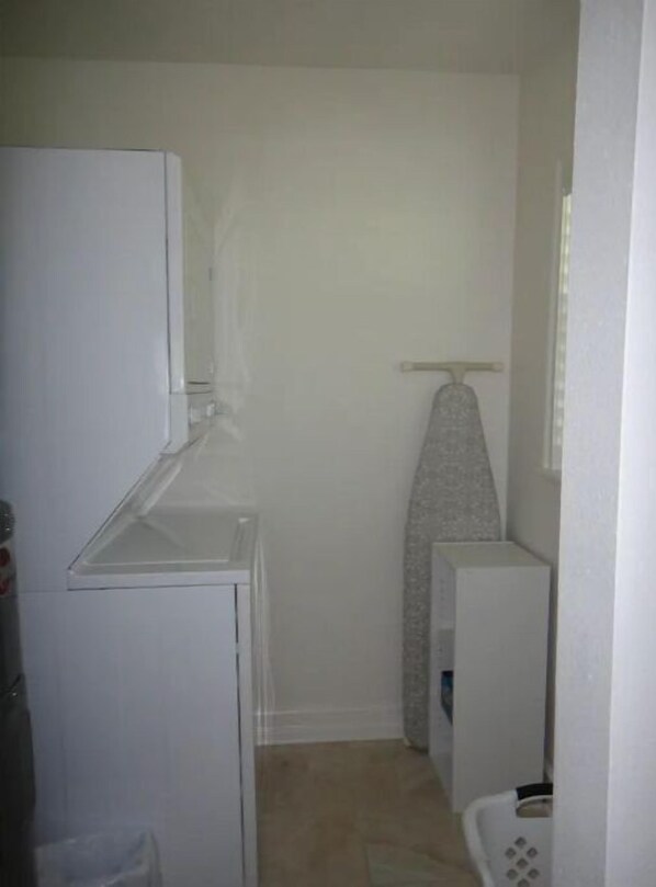 Een kleine keuken met een koelkast, een wasmachine en een strijkplank.