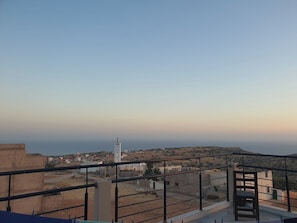 A balcony with a metal railing, a view of a town with buildings and a tower, and a clear sky. - Taghazout : charming house between sea and mountains.  (Taghazout)