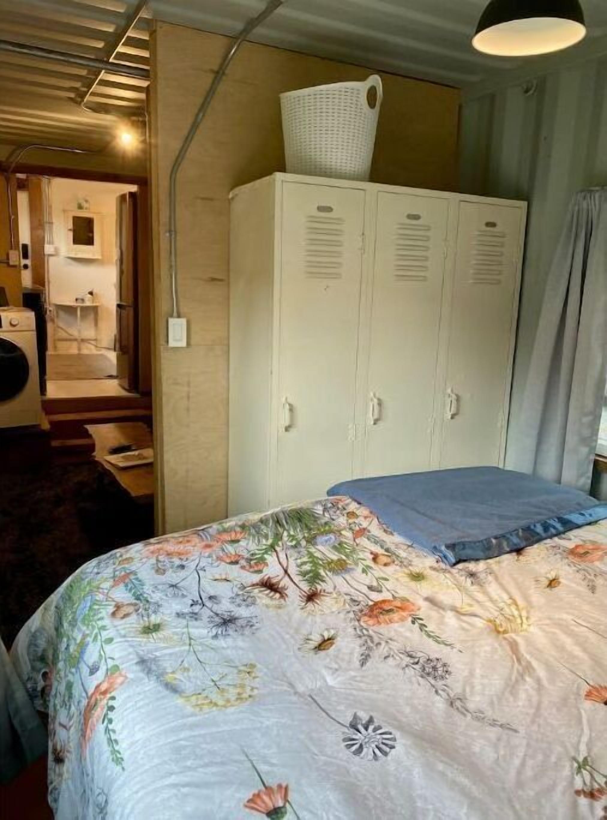 Un dormitorio con una colcha de flores, un armario blanco y una cesta encima.