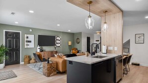 A modern kitchen with a central island, a dining area with a table and chairs, and a living room with a sofa and a coffee table. - 3BR Boho Design | Fire Pit | Steps to Beach (North Myrtle Beach)