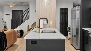 A modern kitchen with a marble countertop, a built-in sink, and a stainless steel refrigerator. - 3BR Boho Design | Fire Pit | Steps to Beach (North Myrtle Beach)