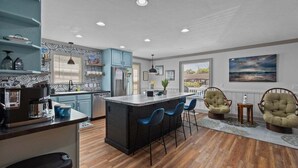 A modern kitchen with a central island, bar stools, and wicker chairs.